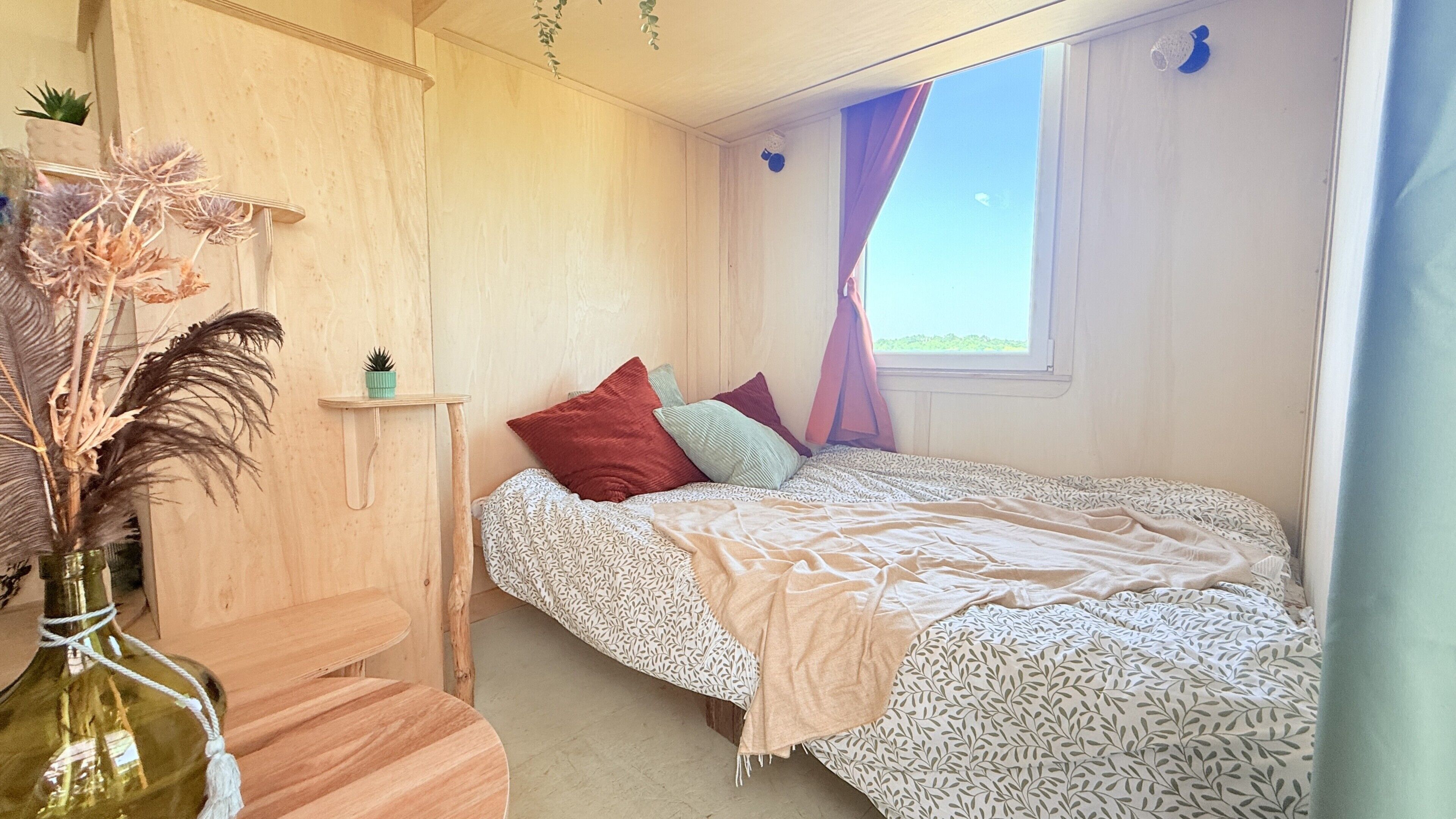 Ein Schlafzimmer mit einem Bett, einem Nachttisch, einer kleinen Ablagefläche und einem Fenster mit Vorhängen.