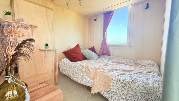 A bedroom with a bed, a bedside table, a small shelf, and a window with curtains.