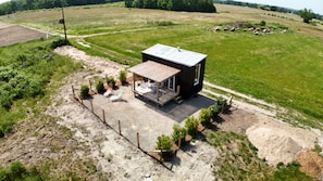 A small cabin with a porch, surrounded by a fenced garden area and open fields. - Unique Accommodations (Montrieux-en-Sologne)