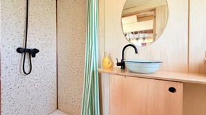 A bathroom with a shower, a sink with a mirror, and a striped curtain.