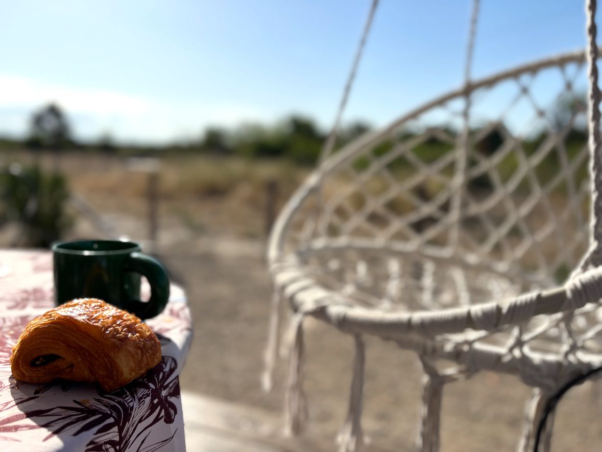 A wicker chair with a tablecloth featuring a floral pattern, a green mug, and a croissant.