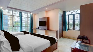 A hotel room with a bed, a desk, a TV, and a window with curtains. - Deluxe Prayagraj Bus Terminal (Prayagraj)