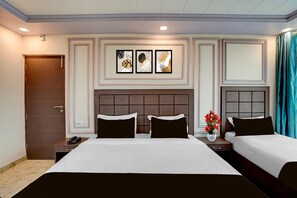 A hotel room with a large bed, two bedside tables, a nightstand, a wall-mounted phone, and a decorative wall panel. - Deluxe Prayagraj Bus Terminal (Prayagraj)