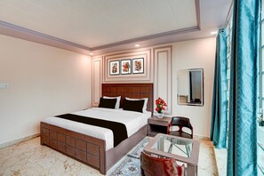 Quarto de hotel com cama, mesa de cabeceira, espelho e uma pequena área de estar com mesa de vidro.