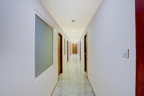 A long, narrow hallway with doors on both sides, leading to rooms. The floor is tiled, and the walls are white. - Deluxe Prayagraj Bus Terminal (Prayagraj)