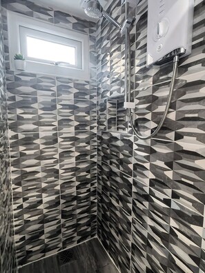 Eine Dusche mit einem geometrischen Fliesendesign, einer Handbrause und einer an der Wand montierten Armatur.