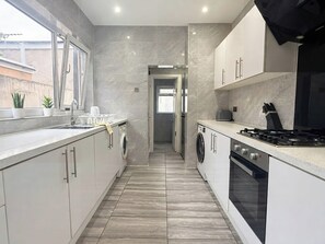 Eine moderne Küche mit Einbauofen, Spüle und Herd. Links befindet sich ein Fenster und eine Tür zu einem weiteren Raum.