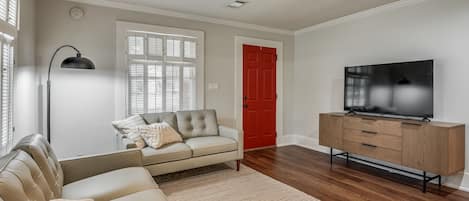 A living room with a sofa, a television, a wooden cabinet, a ceiling fan, and a window with blinds.