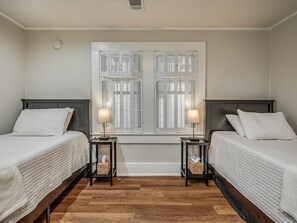 Ein Hotelzimmer mit zwei Betten, einem Fenster mit Rollläden, einem Nachttisch mit Lampe und einem Wandwecker.