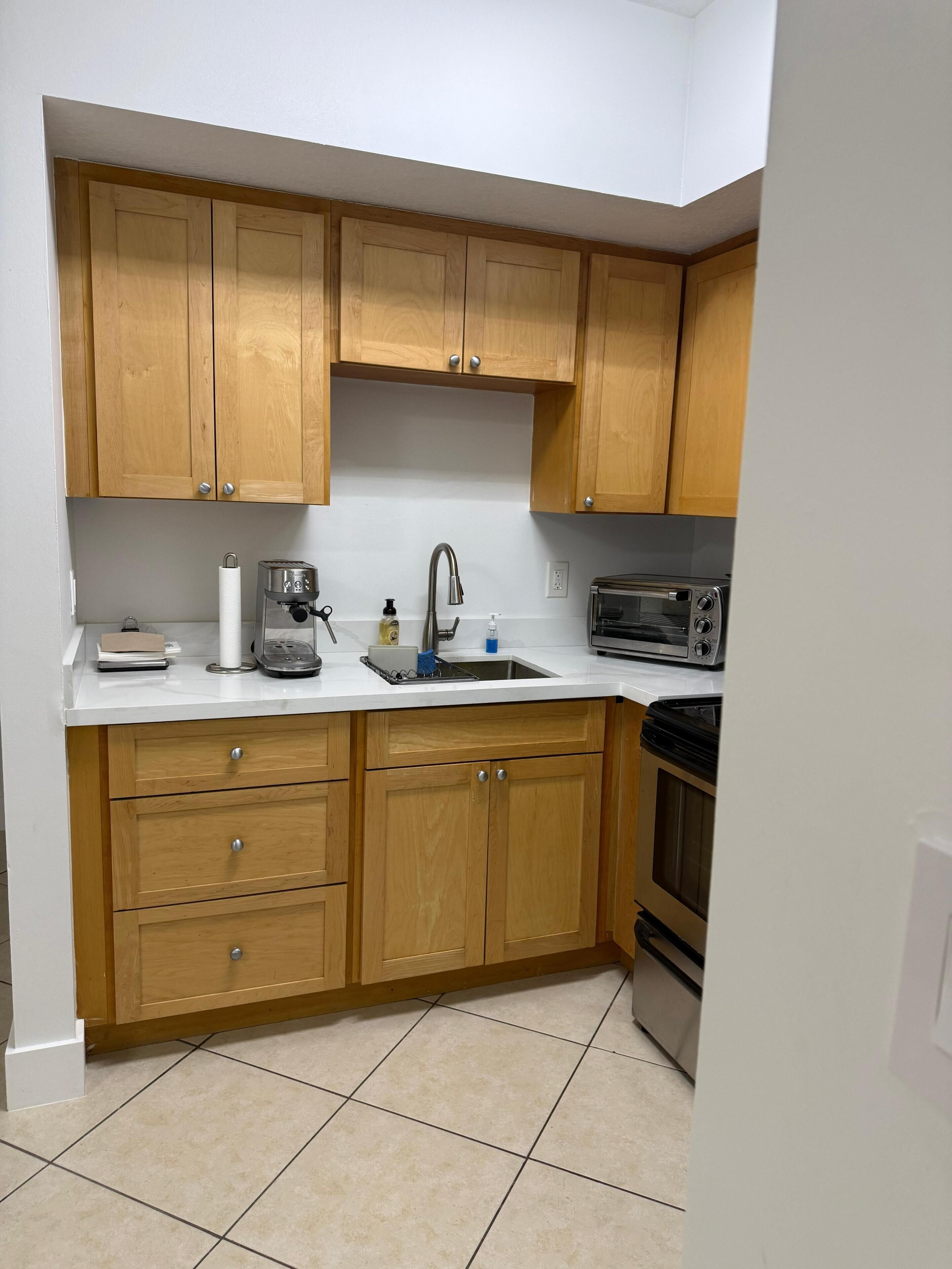 A kitchen with wooden cabinets, a white countertop, a sink, a coffee maker, a toaster, and a microwave.