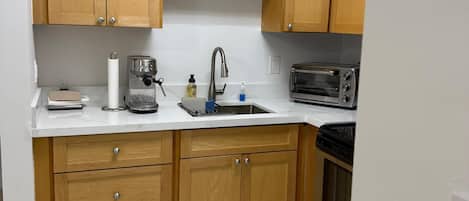 A kitchen with wooden cabinets, a white countertop, a sink, a coffee maker, a toaster, and a microwave.