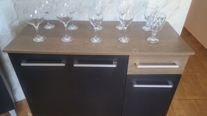 A wooden kitchen counter with six wine glasses and two black cabinets with silver handles.