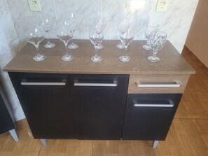A wooden kitchen counter with six wine glasses and two black cabinets with silver handles.