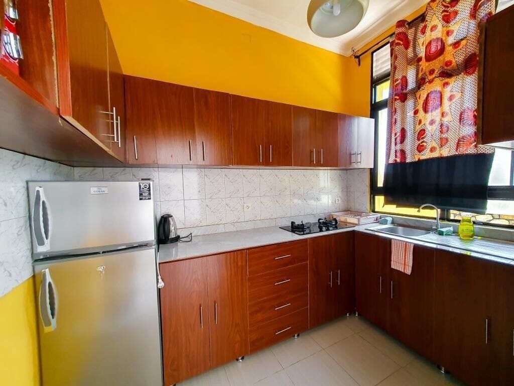 A kitchen with wooden cabinets, a refrigerator, a stove, and a window with a curtain.