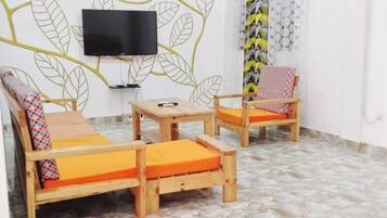 A room with a sofa, two wooden chairs, a small table, and a television mounted on the wall.