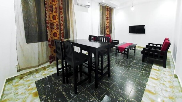 A room with a dining table, chairs, a bench, a TV mounted on the wall, and patterned curtains.