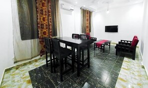 A room with a dining table, chairs, a bench, a TV mounted on the wall, and patterned curtains.