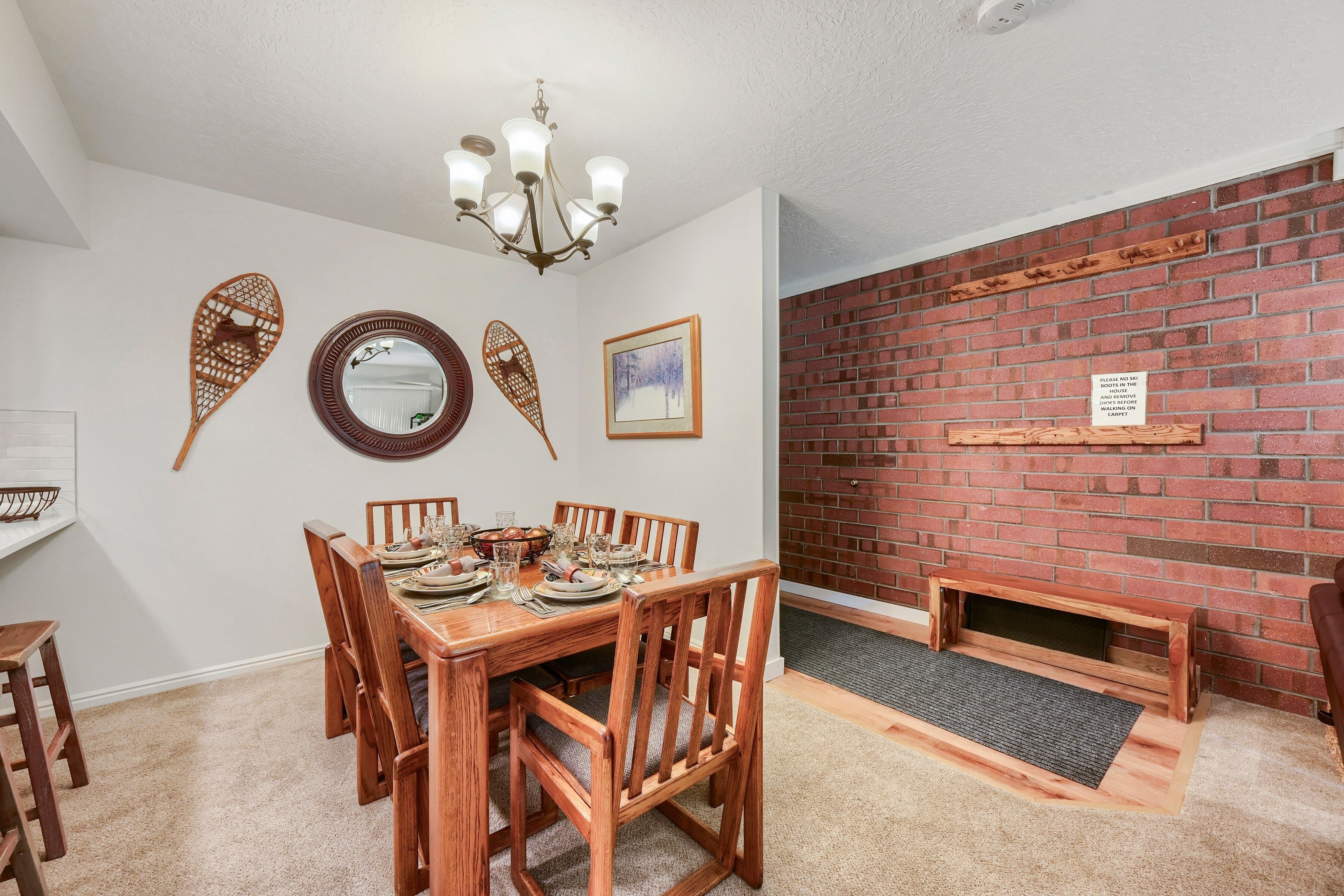 Comedor con una mesa de madera dispuesta para cuatro personas, sillas, una lámpara de araña y decoración en las paredes.