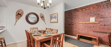 Comedor con una mesa de madera dispuesta para cuatro personas, sillas, una lámpara de araña y decoración en las paredes.