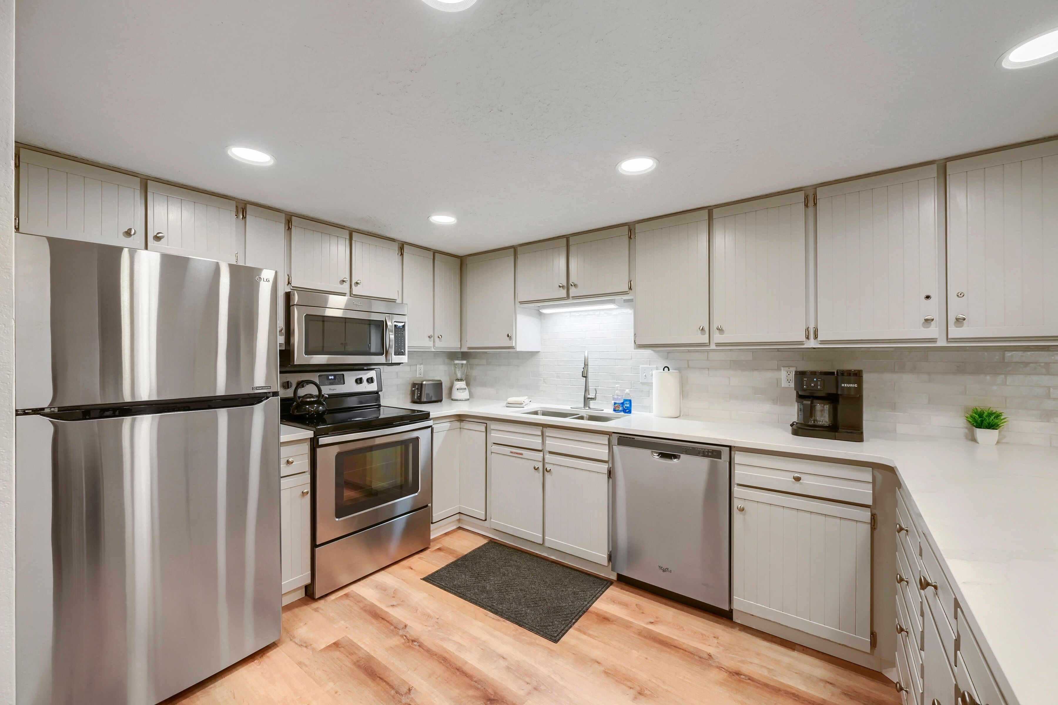A modern kitchen with stainless steel appliances, white cabinetry, and a wooden floor.