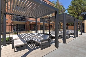 Ein überdachter Außenbereich mit modernem Design, ausgestattet mit einer Couch und Sesseln unter einer Pergola.