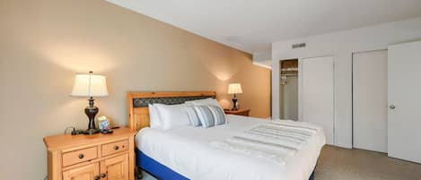 Um quarto com uma cama, duas mesas de cabeceira com abajures, uma mesinha de madeira, um guarda-roupa e um armário.