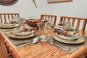 Ein Holztisch ist gedeckt mit Tellern, Schüsseln, Besteck und Gläsern, dazu ein Korb mit Brot und eine Karaffe Wasser.