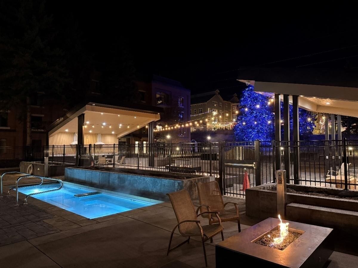 An outdoor pool area with a hot tub, seating, and a fire feature.