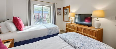 Ein Hotelzimmer mit zwei Betten, einem Fernseher, einer Holzkommode und einem Fenster mit Blick auf Gebäude.