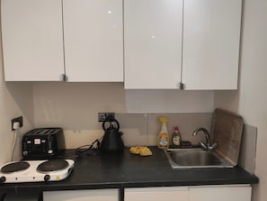 Eine Küche mit weißen Schränken, einer schwarzen Arbeitsplatte, einem Wasserkocher, einem Toaster, einer Spüle und Reinigungsmitteln.