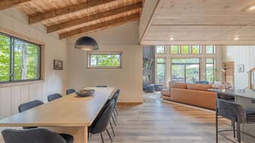 Un comedor amplio con una mesa larga y sillas, una zona de cocina con mostrador y taburetes, y un espacio de descanso con sofá y sillones.