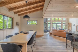 Ein geräumiger Essbereich mit einem langen Tisch und Stühlen, eine Küchenzeile mit Arbeitsfläche und Barhocker sowie eine Sitzecke mit Sofa und Sesseln.