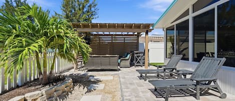 An outdoor patio with a pergola, lounge chairs, and a dining area.