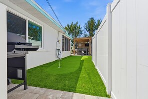 A compact outdoor area with artificial grass, a barbecue grill, and a wooden pergola. - Salt & Surf Cottage - Charming 2-bed house on Anna Maria Island w/ putting green (Holmes Beach)