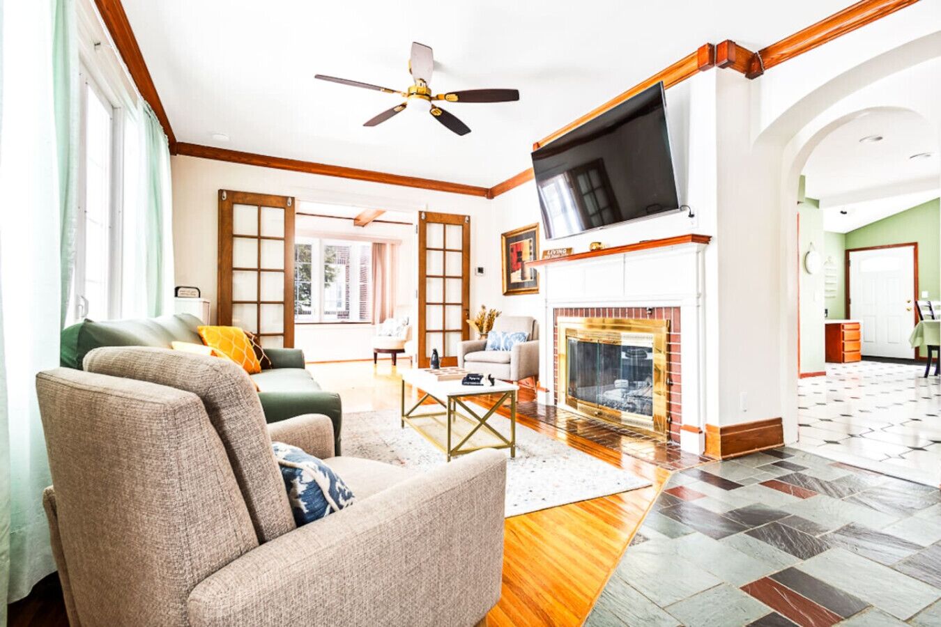 A spacious living room with a fireplace, a ceiling fan, and a large TV mounted on the wall.