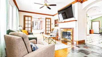 A spacious living room with a fireplace, a ceiling fan, and a large TV mounted on the wall.