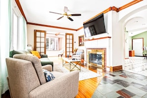 A spacious living room with a fireplace, a ceiling fan, and a large TV mounted on the wall. - Spacious 4BR Near Niagara Falls | Great Location (Niagara Falls)