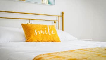 A bed with a gold headboard, white bedding, and a yellow pillow with the word 'smile' on it.