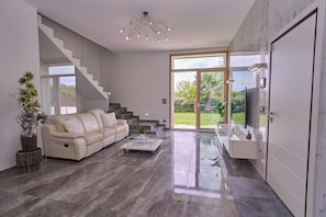 A modern living room with a sofa, coffee table, and a staircase leading to a balcony. - For Families & Relaxation: SUNSTYLEHOUSE in Rimini with a fenced-in garden and parking (Emilia-Romagna)