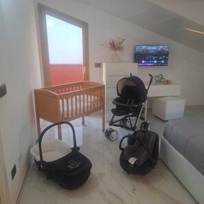 A baby room with a crib, a stroller, a changing table, and a television on the wall. - For Families & Relaxation: SUNSTYLEHOUSE in Rimini with a fenced-in garden and parking (Emilia-Romagna)