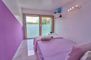 A bedroom with a bed, a nightstand, a shelf with decorative items, and a sliding glass door leading to a balcony. - For Families & Relaxation: SUNSTYLEHOUSE in Rimini with a fenced-in garden and parking (Emilia-Romagna)