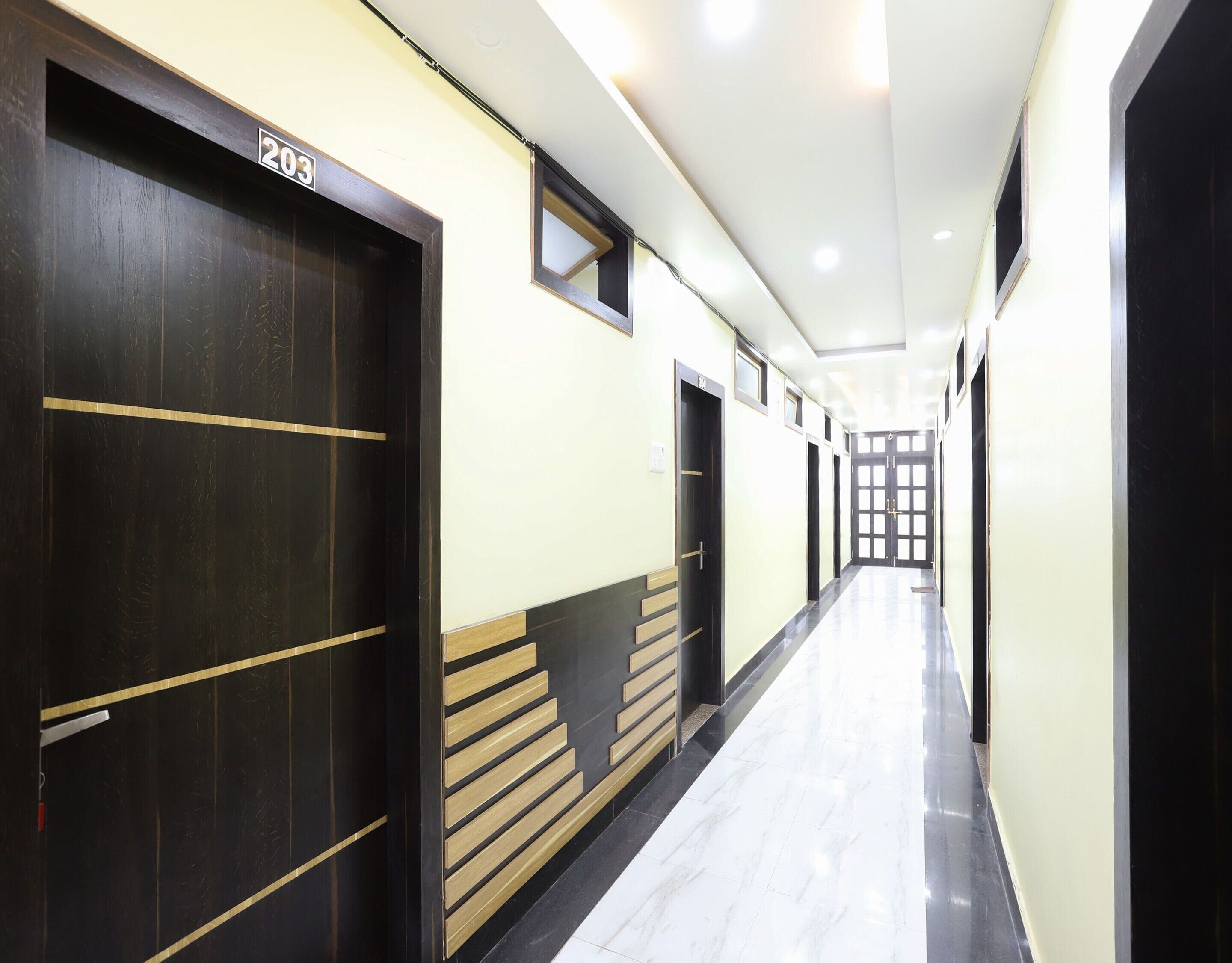 A hallway with doors marked with numbers, a tiled floor, and a light-colored wall.