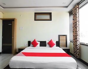 A hotel room with a bed, a nightstand, a mirror, and a window with curtains.