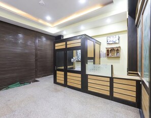 Un área de recepción con mostrador, una puerta con persiana cerrada y una vitrina con fotografías en la pared.