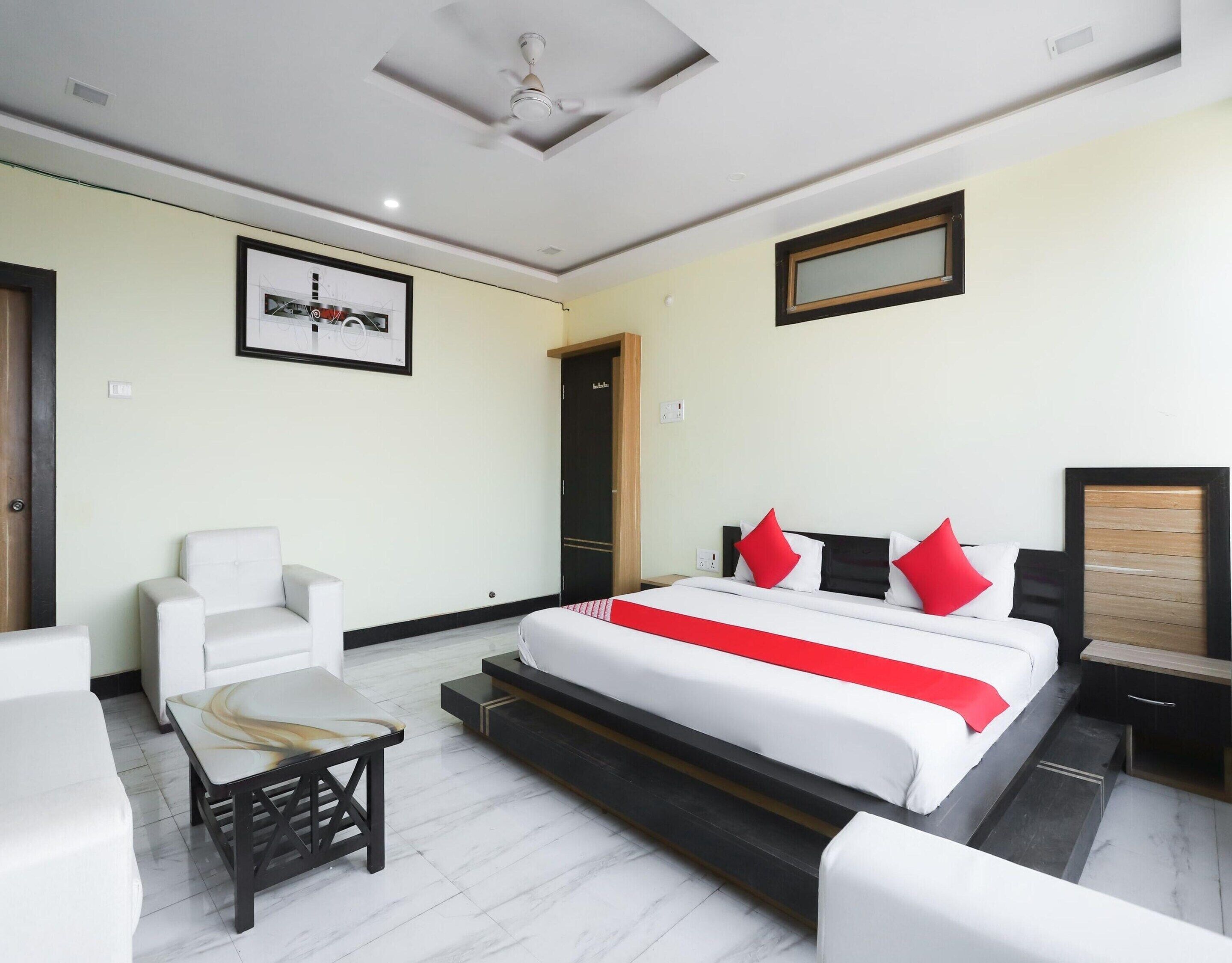 A hotel room with a bed, a chair, a small table, and a ceiling fan.
