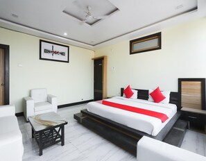 Una habitación de hotel con una cama, una silla, una mesita y un ventilador de techo.