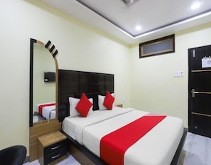 Una habitación de hotel con cama, mesita de noche de madera, espejo, armario y una lámpara en el techo.