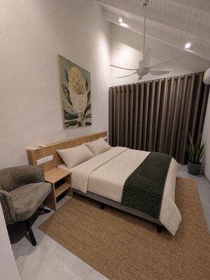 Een moderne slaapkamer met een bed, een stoel, een plafondventilator, een schilderij en een potplant.