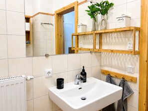 Un baño con un lavamanos blanco, estantes de madera, un espejo y un radiador.