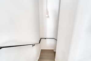 Eine schmale Treppe mit schwarzem Geländer und einer Leuchte darüber.